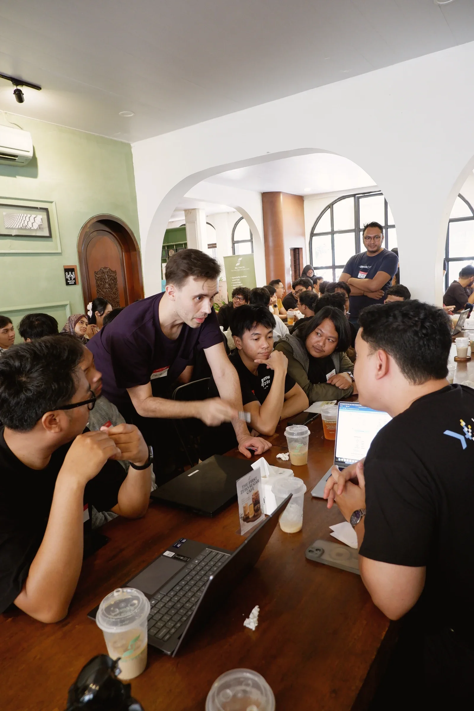 Meetup participants gathered around laptops, with one person leaning forward in conversation