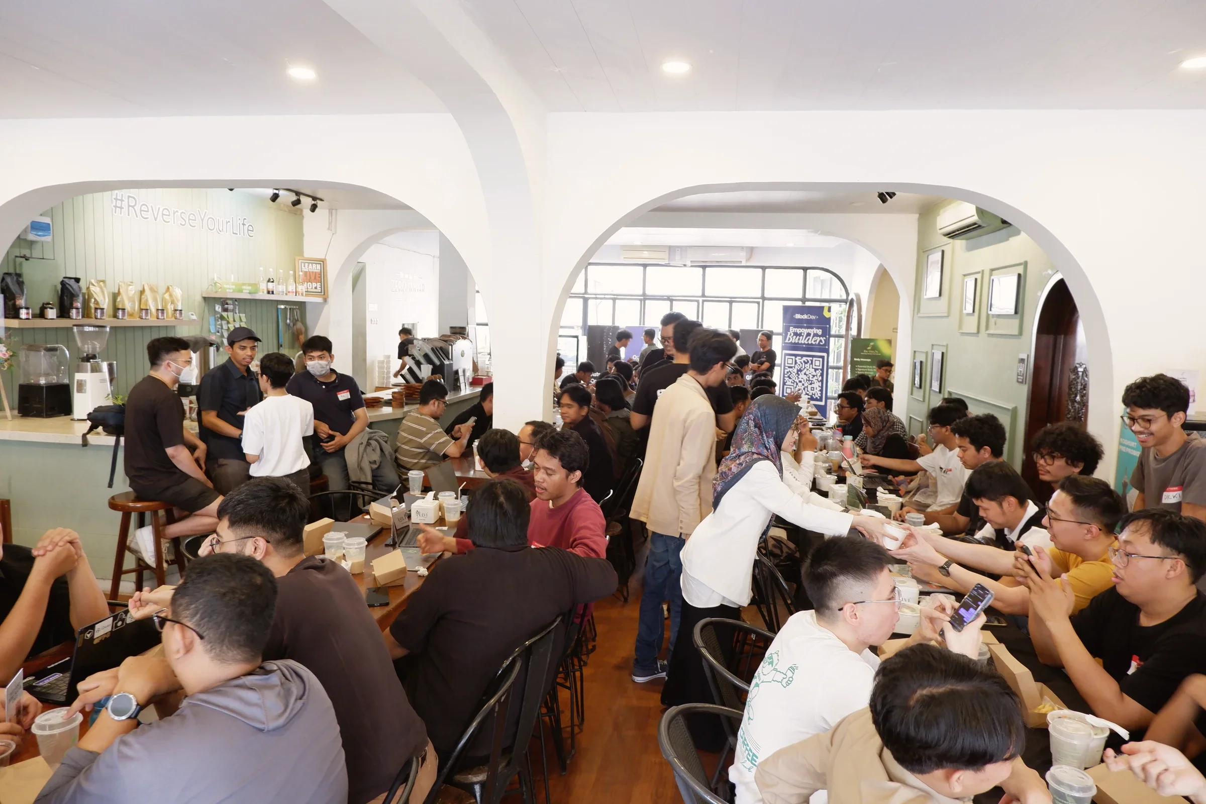 A wide view of Codex meetup participants talking around tables beneath white arches