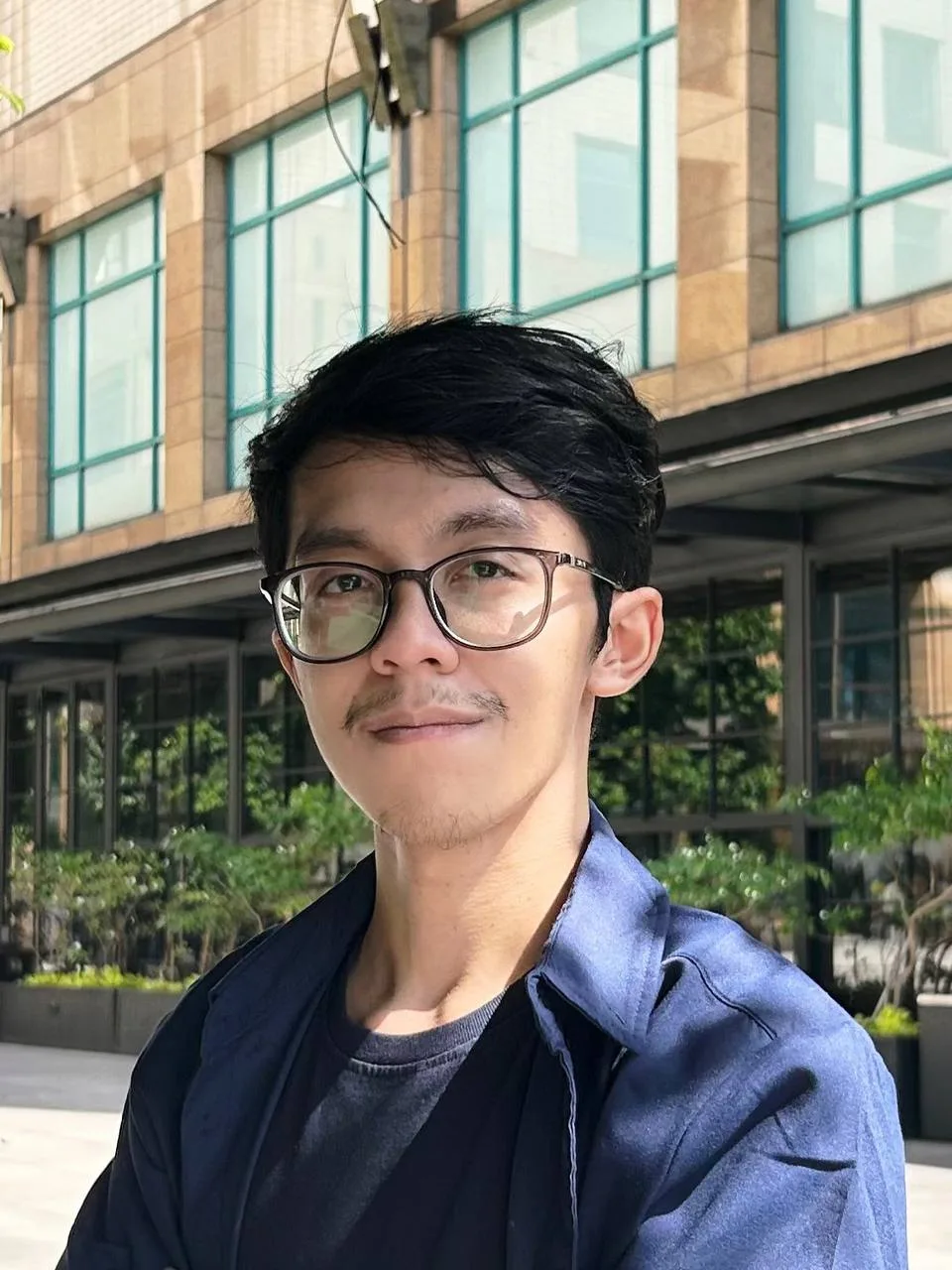Faldi outside a building, wearing glasses and a blue shirt